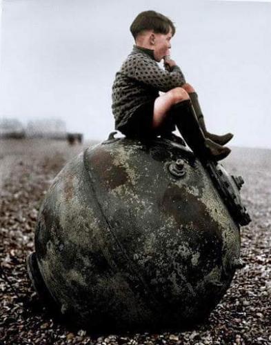 Evacuee Barrie Peacop enjoys an ice cream as he sits on a mine washed up on the beach at Deal in Kent, 7th February 1940. [Colorized]