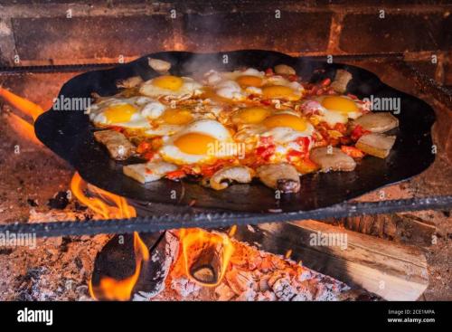 eggs-are-fried-on-a-fire-in-the-street-fried-eggs-with-bacon-a-dish-of-many-fried-eggs-on-a-bonfire-in-the-oven-street-food-rest-with-food-grille-2CE1MPA