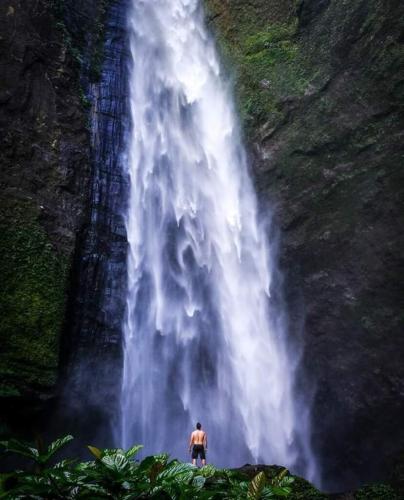 Man looking up at tall waterfall