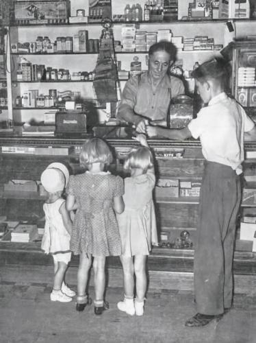 Behind the counter, Henry Alfred Stauffer sells candy to Carlene Bird, Ila Baker, Yvonne Bird and Phillip Humphreys, Mendon, Utah, 1940.